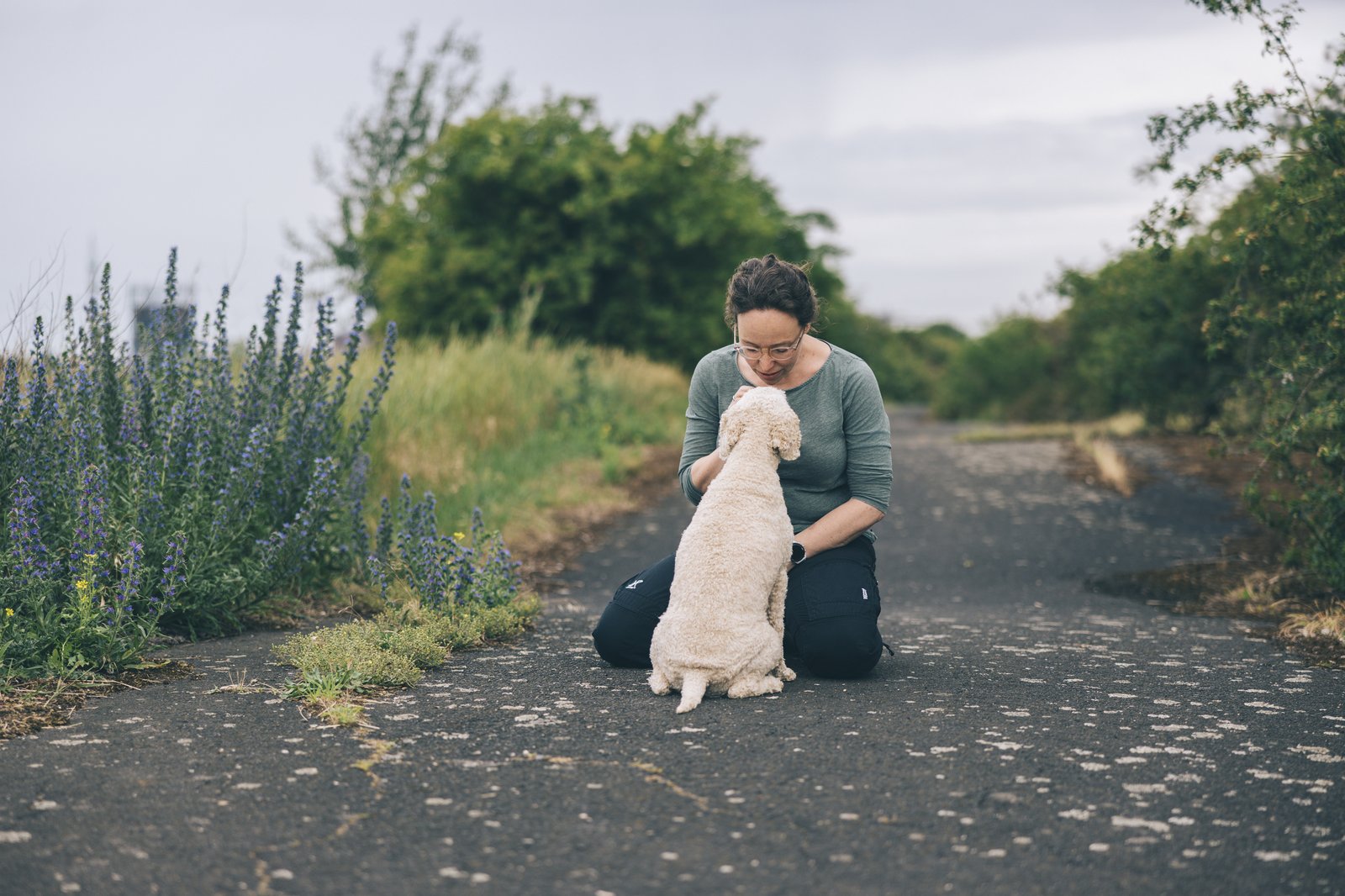 Marina kniet auf einem Feldweg, ihr Hund Maila schaut vertraut zu ihr auf